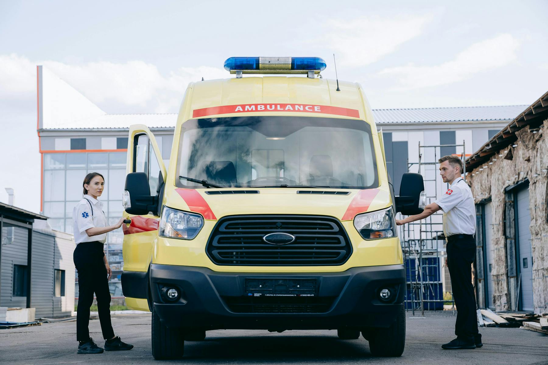 Paramedics standing beside a yellow ambulance in a professional response setting.
